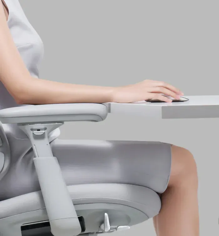 Ergonomik kresloda o'tirgan qiz, qo'li stol bilan bir balandlikdagi tirsakqo'ygichda